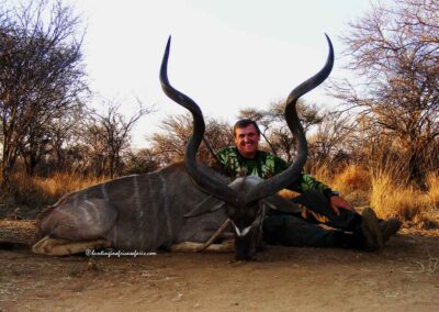A smiling hunter posing with a massive 61-inch Greater Kudu Tragelaphus strepsiceros trophy.