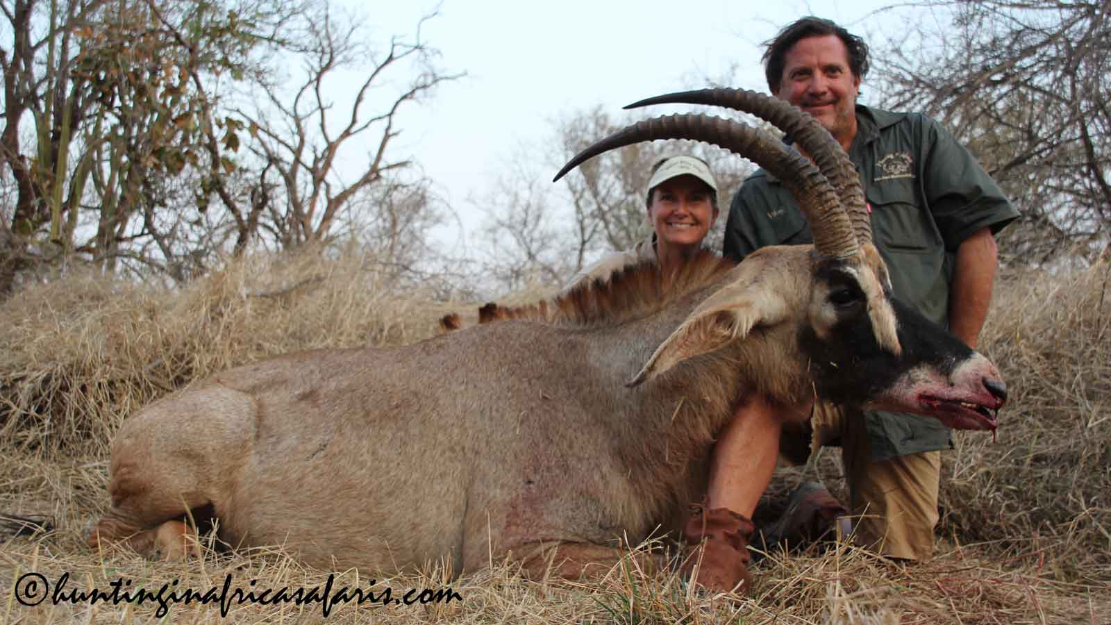 Roan antelope hunting trophy couple A hunter and his wife posing with a trophy roan antelope bull in the South African savanna.